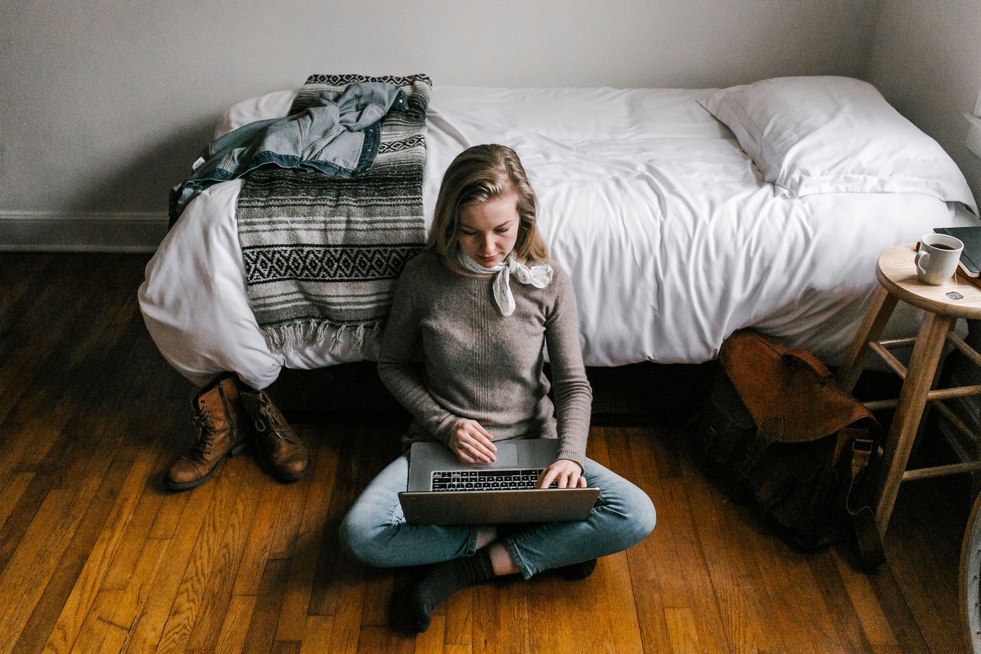 A woman sitting cross-legged on her bedroom floor, working on a laptop